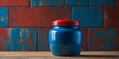 A blue jar with a red lid sits on a table in front of a colorful wall. photo
