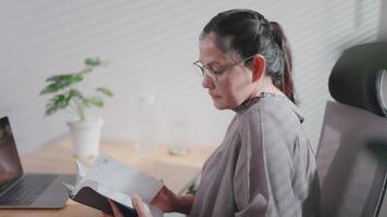 Woman sitting at desk with open window drinking coffee and reading a book enjoying the morning rainbow. video