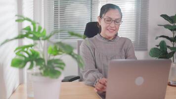 Asian woman typing on laptop in kitchen Business woman working from home smiling looking at website, shopping online, web store, sending message via email. video