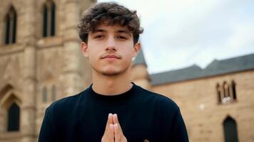 A young man stands tall and proud against the backdrop of a centuriesold church his hands folded in front of him as he takes in the beauty and history of the structure. He. video