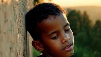 A teenage boy his dark skin glistening with sweat and a look of focus in his eyes as he navigates a difficult route on the outdoor climbing wall the verdant trees and rocky cliffs. video
