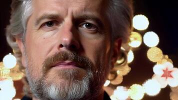 A man in his forties with a saltandpepper beard fixes his gaze on the camera the lights and glittering stars of a holiday stage production serving as the perfect backdrop for the. video