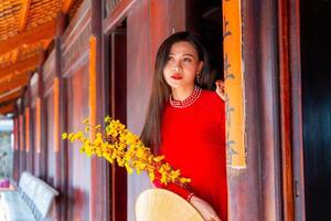 Vietnamese girl with Ao Dai dress standing in traditional house of Vietnam. Text in photo mean best wishes to family, happiness, prosperity, health. Tet holiday and New Year.