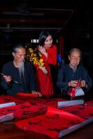 Vietnamese girl with red Ao Dai dress and old scholars writing calligraphy at lunar new year. Calligraphy is a popular tradition during Tet holiday. Text in photo mean Happy New Year and Peace.