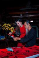 Vietnamese girl with red Ao Dai dress and old scholars writing calligraphy at lunar new year. Calligraphy is a popular tradition during Tet holiday. Text in photo mean Happy New Year and Peace.
