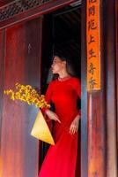Vietnamese girl with Ao Dai dress standing in traditional house of Vietnam. Text in photo mean best wishes to family, happiness, prosperity, health. Tet holiday and New Year.