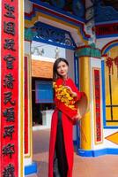 Vietnamese girl with Ao Dai dress standing in traditional house of Vietnam. Text in photo mean best wishes to family, happiness, prosperity, health. Tet holiday and New Year.