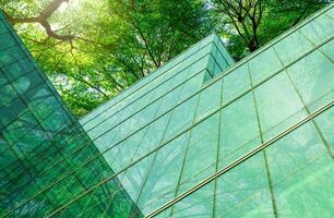 Eco-friendly building in modern city. Sustainable glass office building with trees for reducing carbon dioxide. Office building with green environment. Corporate building reduce CO2. Net zero emission photo