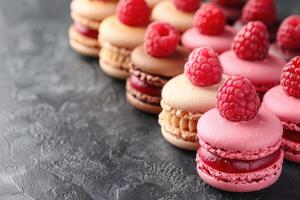 A row of colorful macarons adorned with fresh raspberries rests on a dark textured surface photo