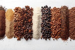 Various types of seeds nuts and spices arranged in separate piles on a white surface photo