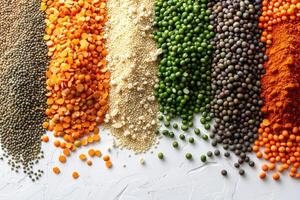Colorful variety of lentils couscous peas and spices arranged in a row on a white surface photo