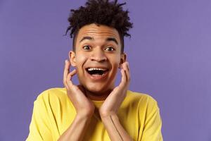 Close-up portrait of extremely happy, enthusiastic young man hear fantastic news, looking surprised and excited, touching face in joy, smiling upbeat look camera astonished, purple background photo