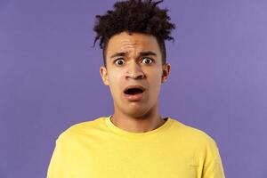 Close-up portrait of shocked, alarmed young man gasping, open mouth scared and frightened, staring camera concerned, facing troublesome shocking news, purple background photo