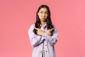 Portrait of indecisive kawaii korean girl in denim jacket, troubled making choice, pouting unsure, look away thoughtful and pointing sideways left and right, choosing between products photo