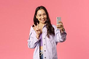 Online lifestyle, people and beauty concept. Stylish pretty korean girl talking to friend online chat, messanger, taking selfie with photo filters app, show peace sign and smiling mobile phone