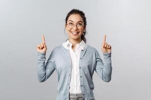 Extremely good news, cant wait to try it. Excited asian girl cant resist temptation, pointing fingers up, looking with interest and desire to try at top advertisement, standing grey background photo