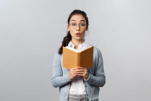 Education, teachers, university and schools concept. Amused and excited asian female tutor reading good homework of student in notebook, fold lips and look camera wondered, grey background photo