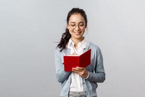 Teaching, education and university lifestyle concept. Smiling smart asian woman in glasses, tutor taking notes, prepare for classes, writing down lecture in notebooks, make schedule in planner photo