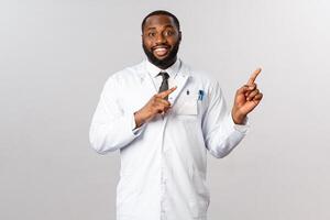 Friendly handsome african-american male doctor explaining main symptoms covid19, showing chart or prescription how be safe, pointing upper right corner and smiling, recommend use face mask photo