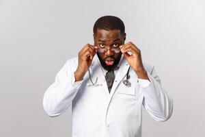 Healthcare, medicine and hospital treatment concept. Impressed and surprised african-american doctor, physician shocked with patient telling his proble, look under forehead with disbelief photo