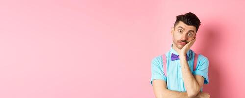 Shocked and tired caucasian guy staring pissed-off at camera, lean on palm and looking at something with skeptical face, standing over pink background photo