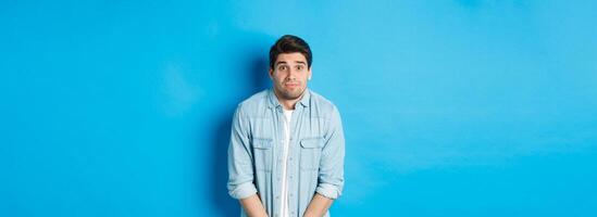 Embarrassed guy want to pee, waiting in line for toilet, standing against blue background photo