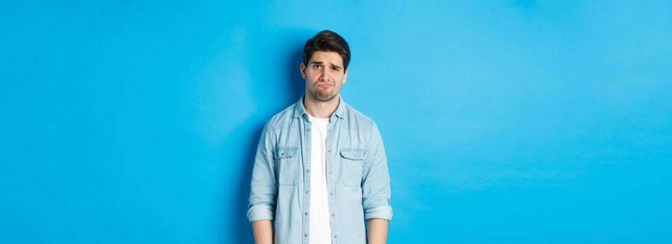 hombre mirando con duda a cámara, ceñudo y enfurruñado, sensación difícil acerca de algo, en pie en contra azul antecedentes foto