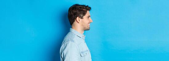 Profile of handsome young man looking left, smiling happy, standing over blue background photo