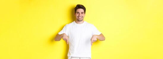 Attractive bearded man pointing fingers down, showing event banner, standing over yellow background photo