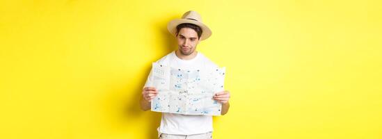 Travelling, vacation and tourism concept. Male tourist looking confused at map, looking for right direction, standing over yellow background photo