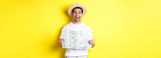 Travelling, vacation and tourism concept. Excited man tourist going sightseeing with map, standing over yellow background photo