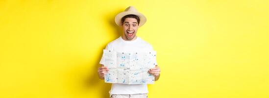 Travelling, vacation and tourism concept. Man tourist looking happy at map with sighsteeings, explore city, standing over yellow background photo