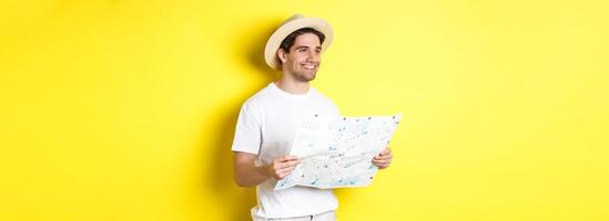 Travelling, vacation and tourism concept. Handsome guy tourist going sightseeing, holding map and smiling, standing over yellow background photo