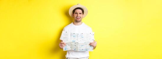 Travelling, vacation and tourism concept. Puzzled guy tourist cant understand map, looking confused at camera, standing against yellow background photo