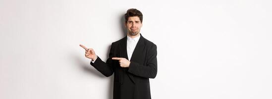 Image of devestated man in party suit, crying and complaining, pointing fingers right at something disappointing, standing over white background photo