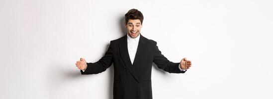 Portrait of excited handsome man in suit, shaping big object on copy space and smiling amazed, holding something, standing over white background photo
