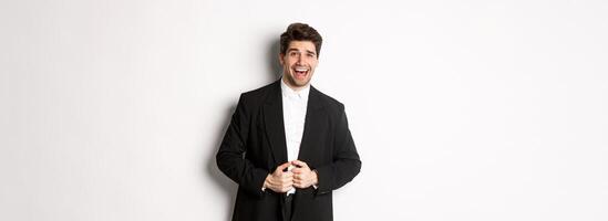 Concept of new year party, celebration and lifestyle. Portrait of handsome and confident man in suit, smiling pleased, feeling successful, standing over white background photo