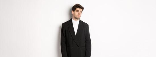 Image of tired man in suit looking left with distressed, gloomy expression, stare left at copy space, standing exhausted over white background photo
