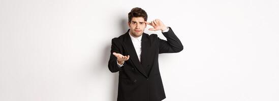 Portrait of confused handsome businessman scolding employee, pointing at head and camera, standing disappointed over white background photo