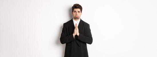 Miserable clingy guy need help, pouting silly and begging for something, asking for favour, standing against white background in black suit photo