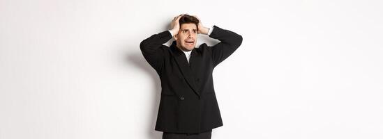 Image of anxious businessman start to panic, looking left with worried expression, standing in black suit over white background photo