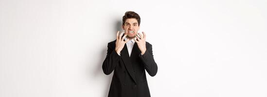 Image of angry businessman in suit, looking with furious expression and clenching fists, express hatred, standing mad over white background photo
