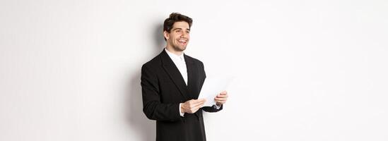 Image of handsome businessman in suit, holding documents and smiling, standing against white background photo
