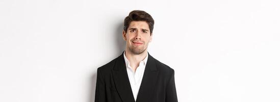 Close-up of confused handsome man in suit, grimacing and looking perplexed, wearing trendy suit, standing against white background photo
