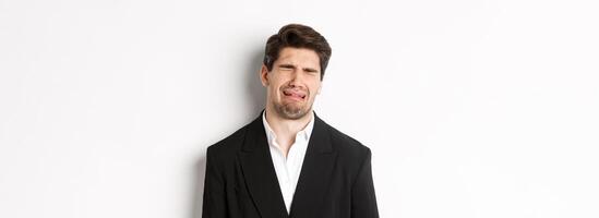 Close-up of miserable man in suit, crying and sobbing, feeling sad, standing against white background photo