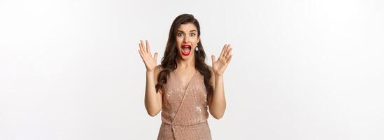 Celebration and party concept. Beautiful woman in elegant dress screaming and staring at camera scared, looking at something scary, standing over white background photo