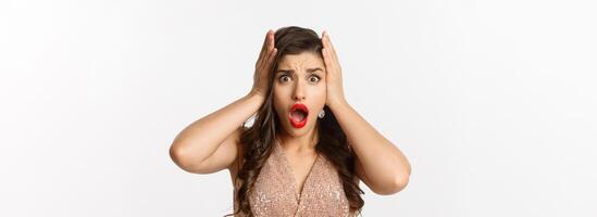 Concept of New Year celebration and winter holidays. Close-up of woman in luxury dress looking shocked and worried, standing over white background photo