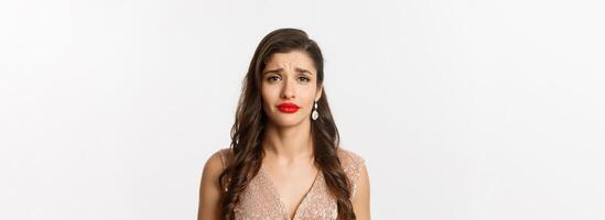 Concept of New Year celebration and winter holidays. Close-up of sad and gloomy woman with hairstyle and red lips, frowning and looking with pity, standing over white background photo