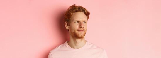 Close up of skeptical and unamused european man, smirk with judgemental face, looking left at banner, standing over pink background photo