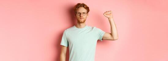 Confident redhead man standing united with black lives matter movemet, showing raised fist and looking serious at camera, protesting and being an activist, standing over pink background photo